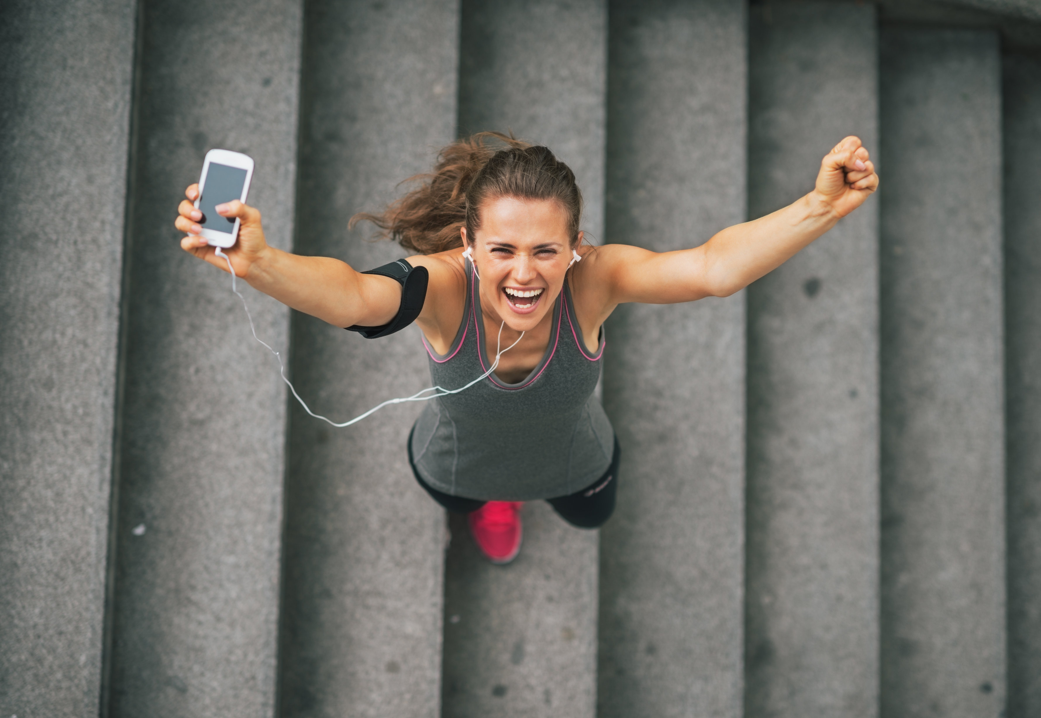 Portrait of happy fitness young woman with cell phone outdoors in the city rejoicing